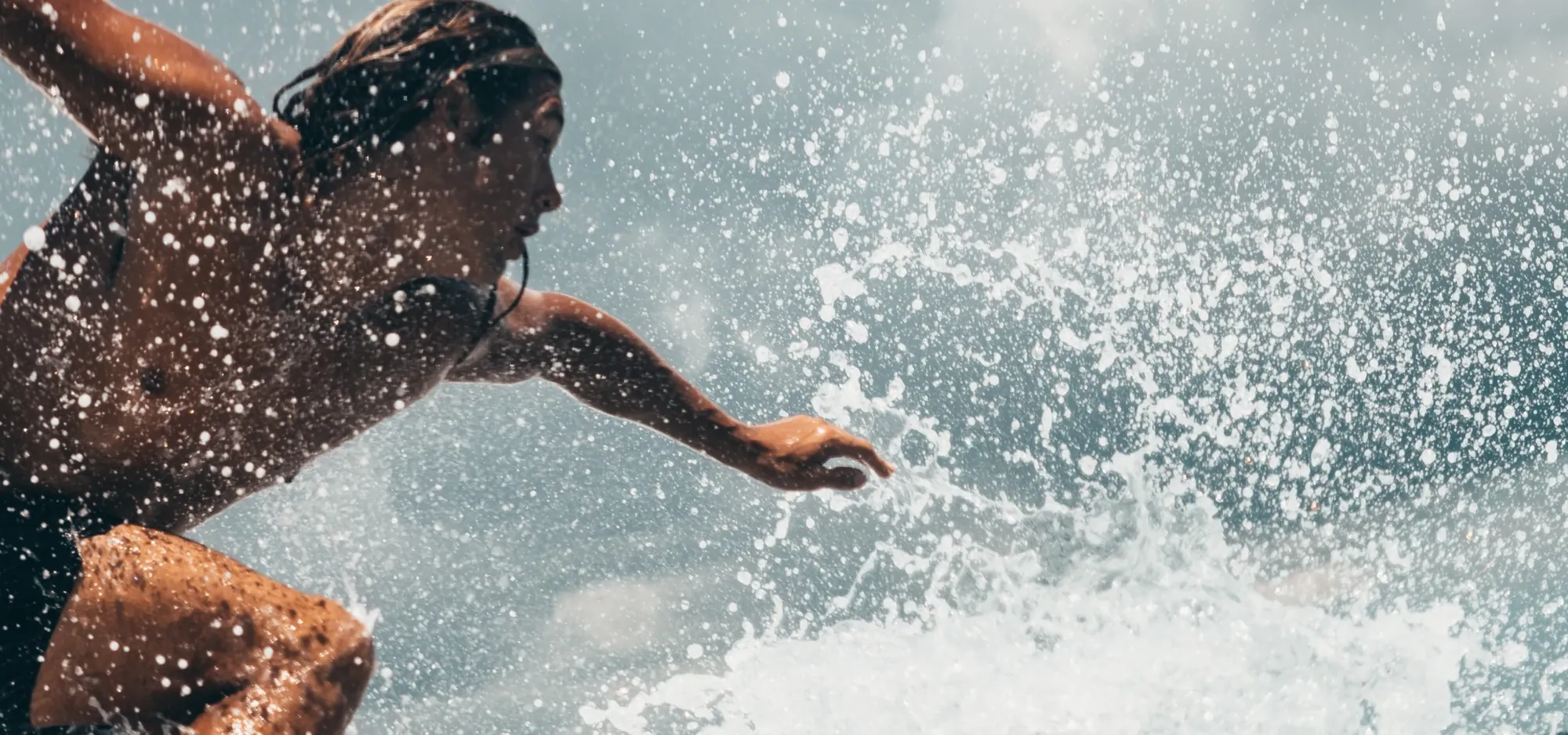A surfer crouched on a wave with one arm reaching out through a burst of spray