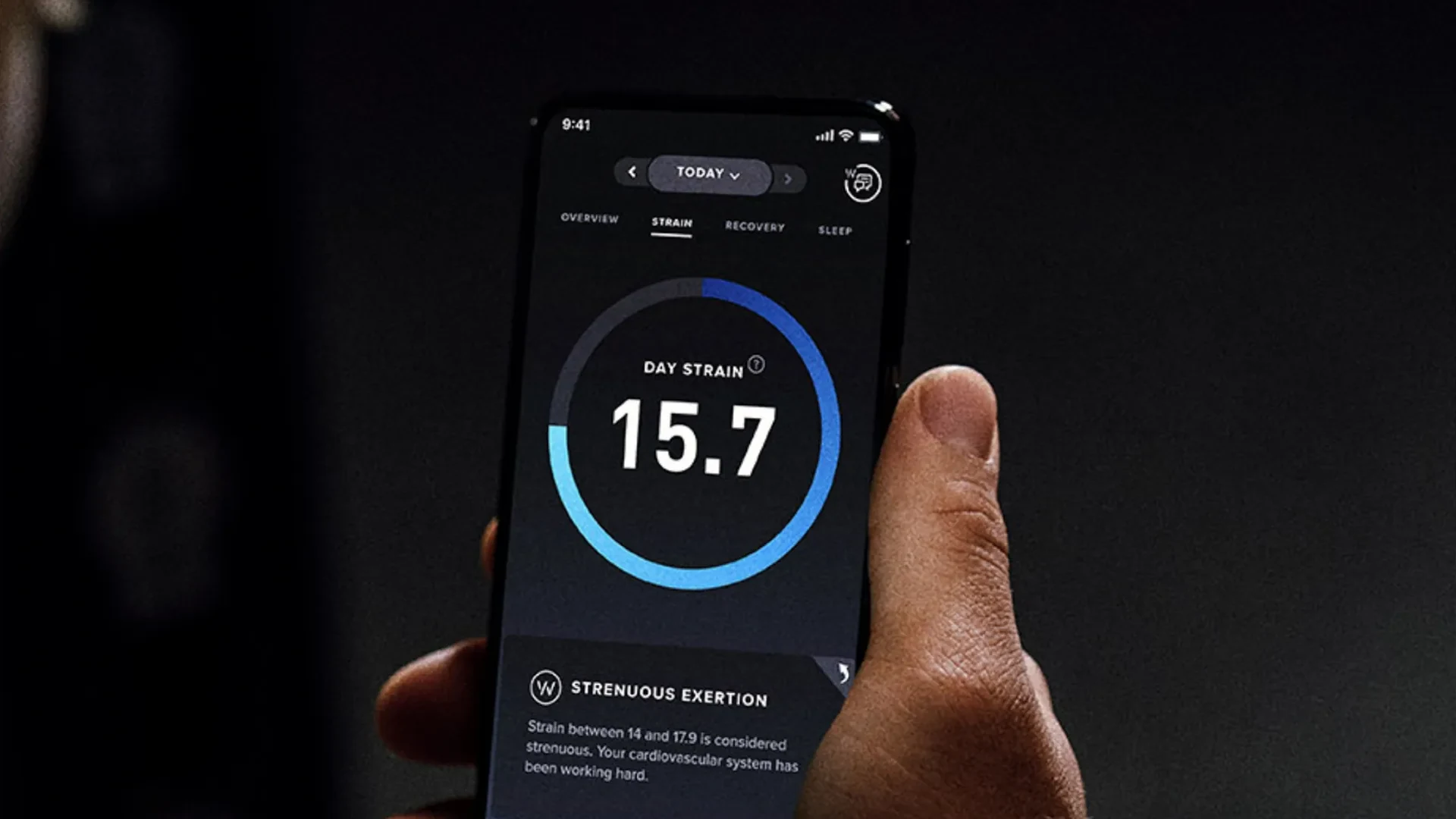 A hand holding a phone open to the Whoop app's Day Strain screen