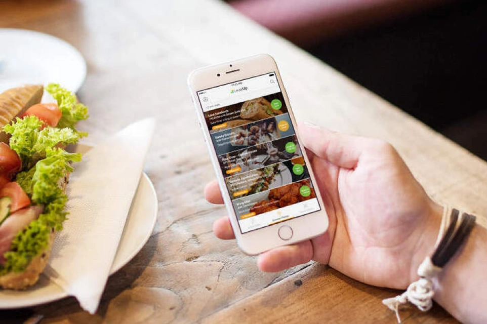 A hand holding a phone with a food ordering app open, beside a plate of salad on a wooden table.